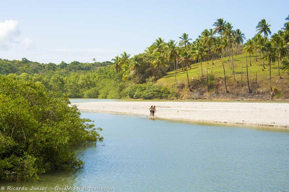 Imagem de casal caminhando na beira da piscina natural.